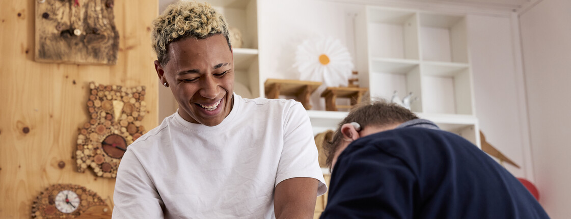 Man sieht einen lachenden Junge und eine weitere Person, die sich in einer Werkstatt befinden.