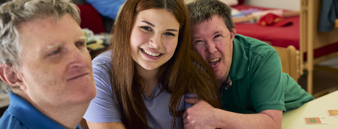 Man sieht drei glückliche Personen, zwei Männer und in der Mitte ein Mädchen.